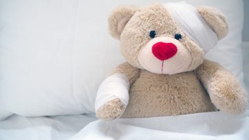 Erste Hilfe bei Kindern: Ein Teddybär ist im Bett und hat einen Verband um seinen Kopf.